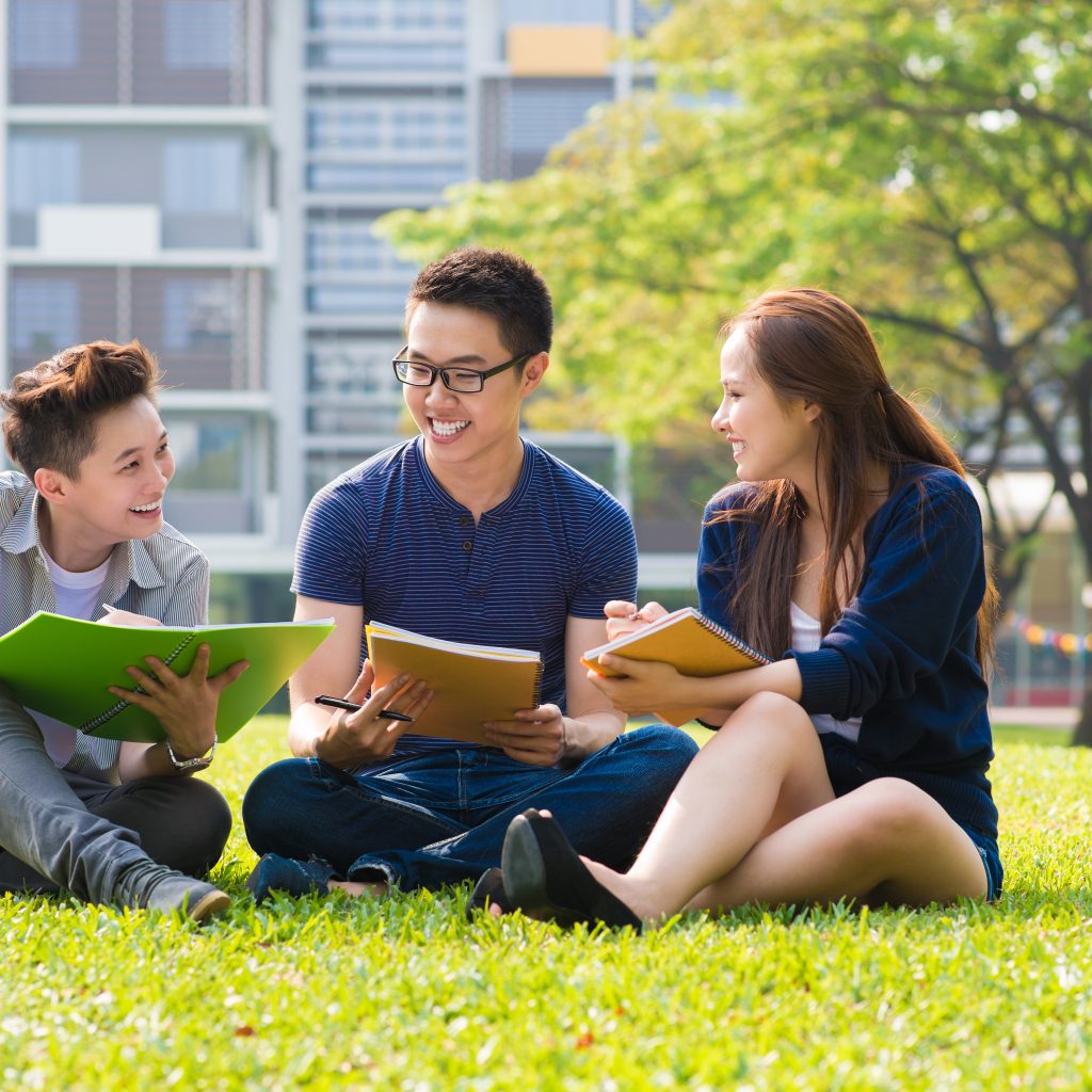 Group of students studying together outdoors, discussing JC Economics concepts and exam strategies in a relaxed setting.