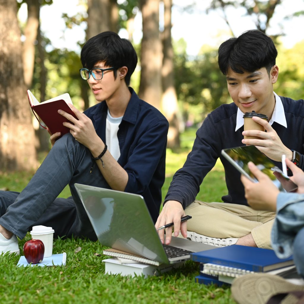 JC students studying together outdoors with laptops and notes, reinforcing concepts and exam readiness through JC economics tuition