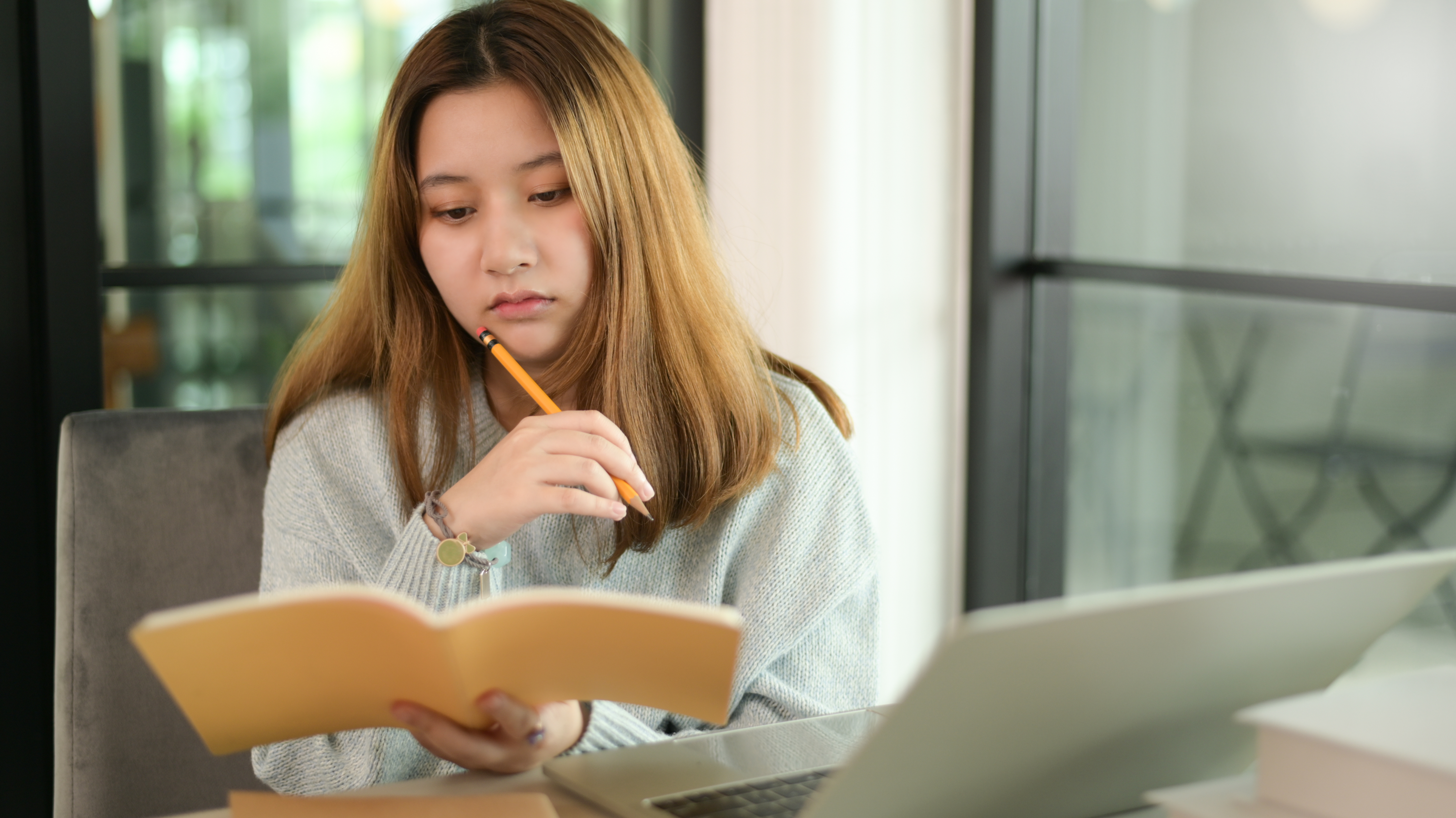 a female student holding a pencil and a notebook thinking of what she should write for her essay